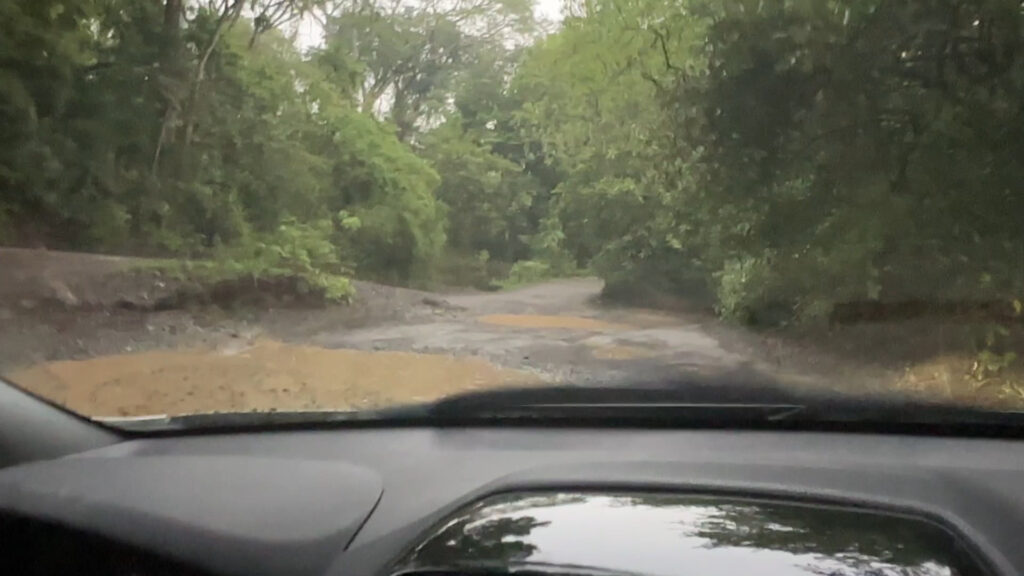 View out of front of car showing dirt road and potholes filled with water