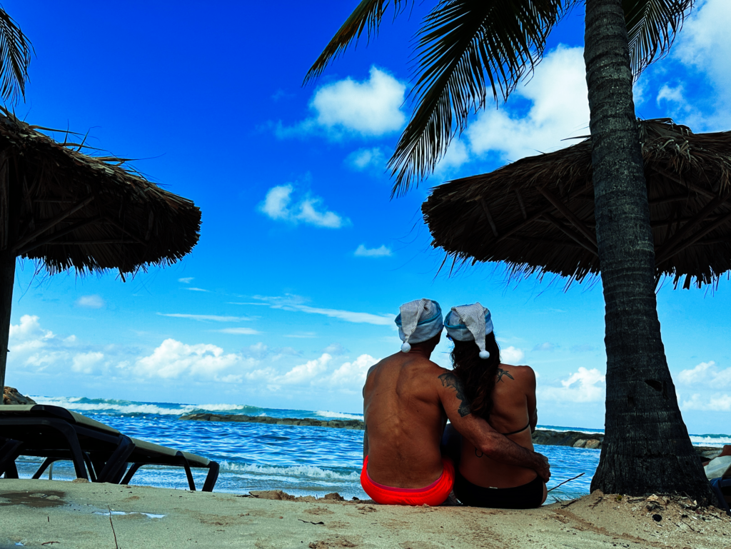 Darren and Julie in Santa hats sitting on beach